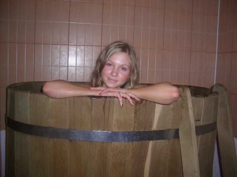 Голая блондинка лежит в деревянной ванне